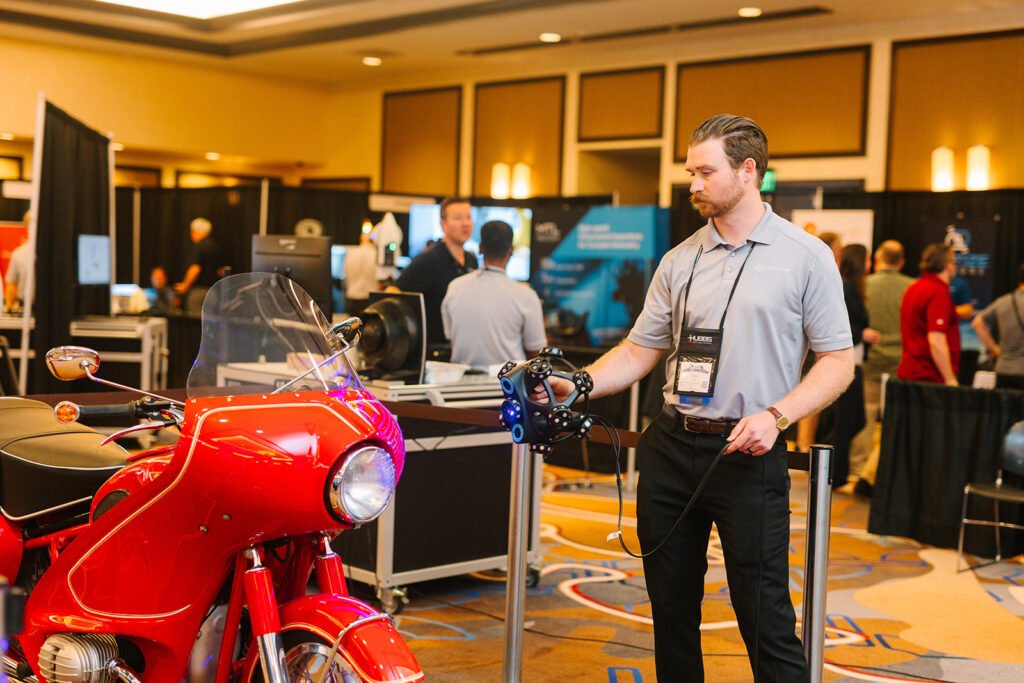 Attendees talking beside a red vintage motorcycle on the CMSC exhibit hall floor