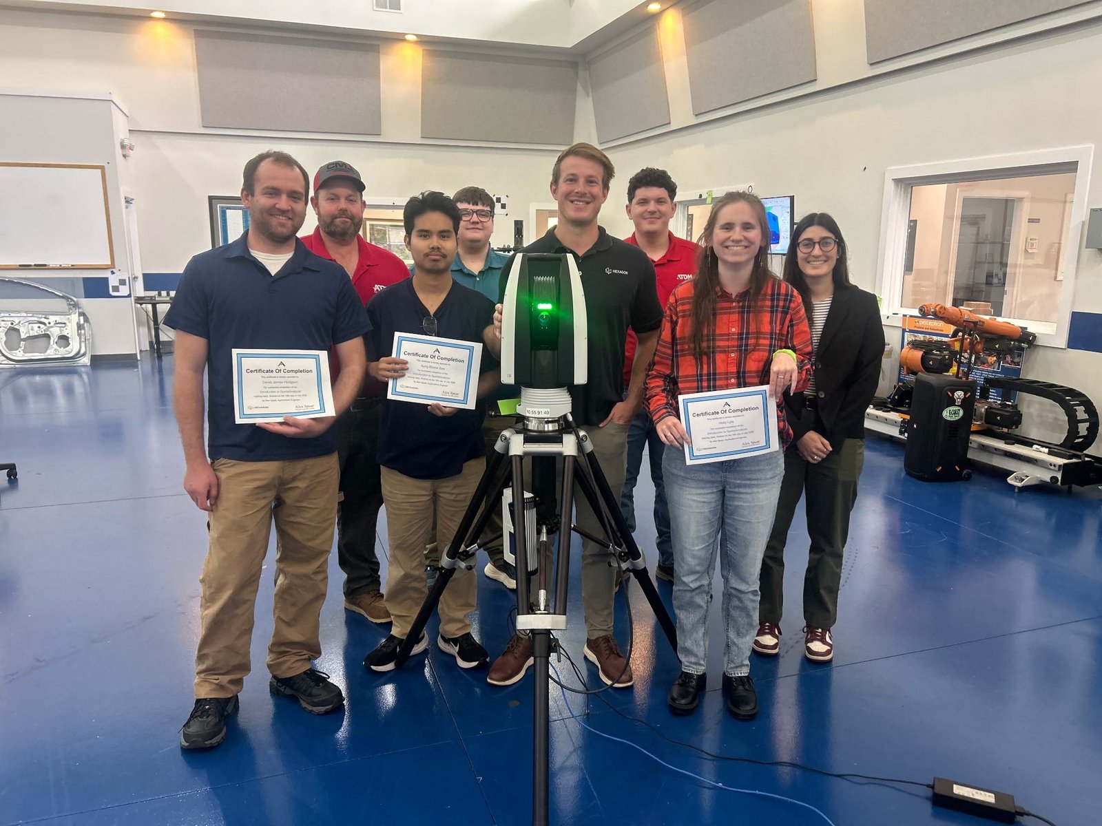 Training participants holding Certificates of Completion for an Introduction to SpatialAnalyzer class beside a laser tracker on a tripod